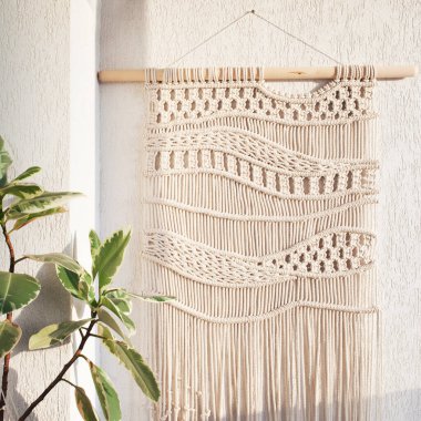 El yapımı makrome. Beyaz bir duvara asılı ahşap sopayla% 100 pamuk duvar süslemesi. Makrame örgü ve pamuk iplikleri. Kadın hobisi. ECO dostu modern örgü DIY doğal dekorasyon konsepti iç mekanda
