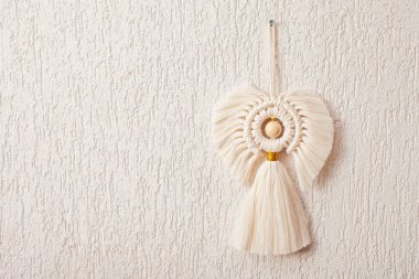 Noel makromu dekoru. Beyaz duvardaki Noel meleği. Doğal malzemeler, pamuk ipliği, tahta boncuklar. Eko dekorasyonlar, süsler, el yapımı dekorasyon. Boşluğu kopyala