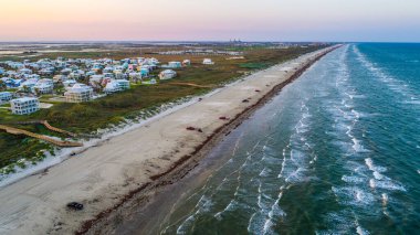 Aerial drone view of paradise island with new development real estate homes and condos along the beach with waves crashing into the horizon near Corpus Christi Texas