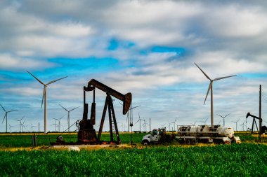 Yenilenebilir enerji yaratan dev rüzgar türbinleri Batı Teksas 'ta petrol pompalayan eski bir petrol platformunu çevreleyerek arka planda yenilenebilir enerji yaratıyor.