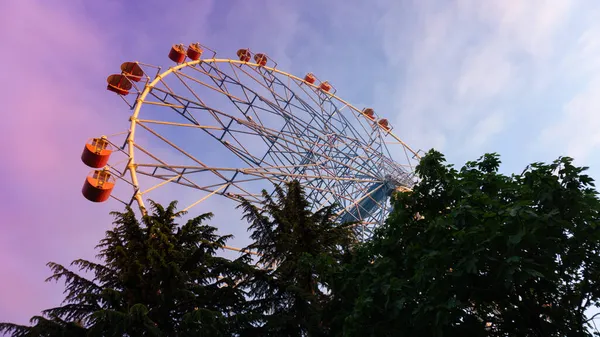 Φωτεινά χρωματιστό τροχό λούνα παρκ ενάντια στο ηλιοβασίλεμα του ουρανού. Lazarevskoye, Sochi, Ρωσία, Στο τιμόνι η επιγραφή Lazarevskoe — Φωτογραφία Αρχείου