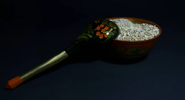 Ωμό μαργαριτάρι κριθάρι σε ένα ξύλινο πιάτο με λαϊκά σχέδια και μια ξύλινη κουτάλα ξαπλωμένη σε ένα μπολ — Φωτογραφία Αρχείου