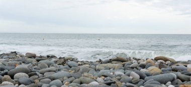 Deniz taşları ve arka planda azgın bir deniz olan küçük çakıl taşları. Yuvarlak pürüzsüz, pürüzsüz bir çakıl taşının yakın çekimi. Seçici odak