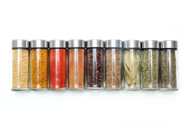 Beyaz arka planda izole edilmiş küçük kapaklı cam şişede saklanan farklı baharat ve otlar..