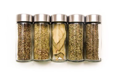 Beyaz arka planda izole edilmiş küçük kapaklı cam şişede saklanan farklı baharat ve otlar..