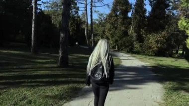 Parkta yürüyen genç sarışın kızın arka görüntüsü..