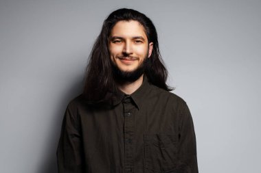 Uzun siyah saçlı, gülümseyen yakışıklı bir adamın portresi..