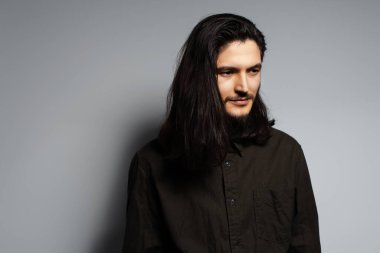 Gri arka planda uzun saçlı genç adamın stüdyo portresi..