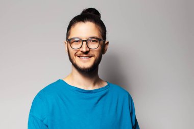 Gri arka planda mavi gömlekli gülümseyen genç adamın stüdyo portresi.