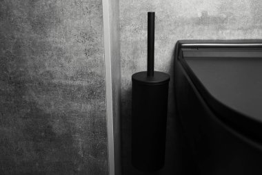 Banyo detaylarının yakın görüntüsü: Siyah duvar monte edilmiş tuvalet ve temizlik fırçası.