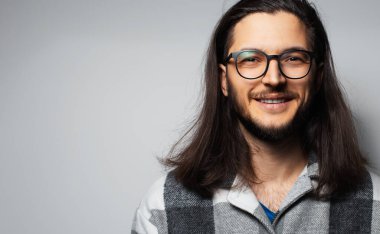 Gri arka planda uzun saçlı, gülümseyen yakışıklı adamın stüdyo portresi..