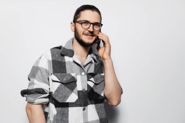 Gri stüdyonun arka planında akıllı telefondan konuşan genç adam..