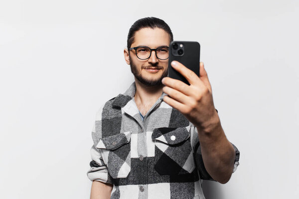 Фото привлекательного молодого парня в клетчатой рубашке, делающего селфи на смартфоне.