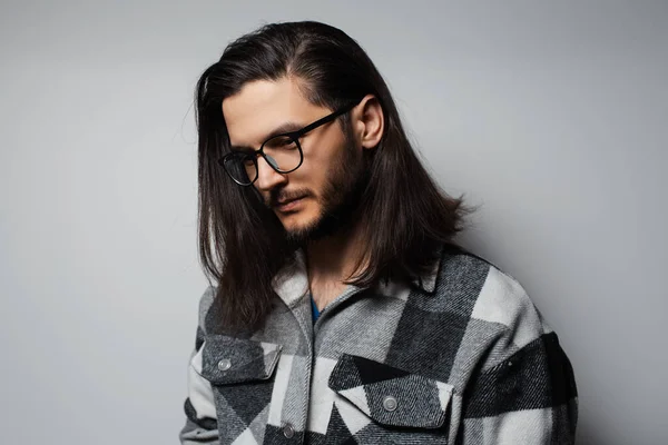 Studio portrait of young handsome guy with long hair, wearing plaid shirt.