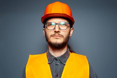 Gri arka planda kendine güvenen bir inşaat işçisi. Stüdyo portresi. Genç adam..