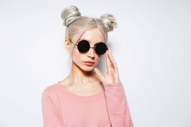 Saçlı çörekleri olan, beyaz güneş gözlüğü takan, ciddi ve şık bir sarışın kız..