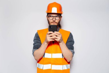 Stüdyo portresi: Beyaz üzerine genç inşaat işçisi, akıllı telefondan mesaj..
