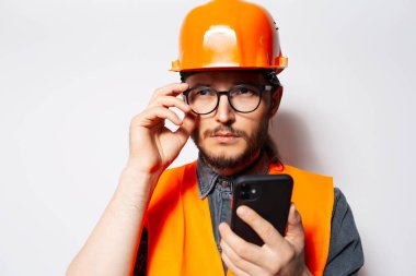 Beyaz arkaplanda akıllı telefon kullanan kendinden emin bir mühendisin portresi.