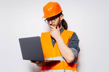 İnşaat işçisi beyaz arka planda dizüstü bilgisayara bakıyor. Turuncu ekipman.