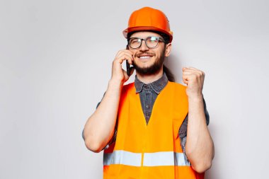 İşte bu! Turuncu ekipmanla akıllı telefondan konuşan mutlu inşaat işçisi.