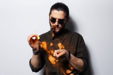 Genç hippi beyaz stüdyo arka planında kibritle sigara yakıyor..