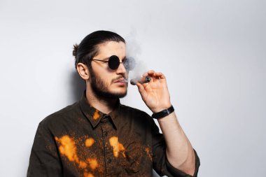 Beyaz arka planda güneş gözlüğü takan, purolu genç bir adamın yan portresi..