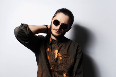 Boynunun arkasında eli beyaz güneş gözlüğü takan ciddi bir genç adam..