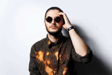 Yuvarlak güneş gözlüğü takan, beyaz arka planlı, ciddi bir genç..