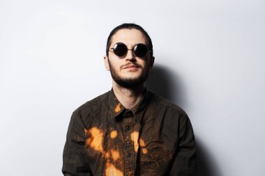 Beyaz arka planda yuvarlak güneş gözlüğü takan kendinden emin genç bir adamın portresi..