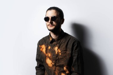 Yuvarlak güneş gözlüğü takan, beyaz arka planda, ciddi bir gencin portresi..