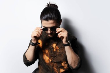 Güneş gözlüklerini beyaz arka planda ayarlayan ciddi bir gencin stüdyo portresi..