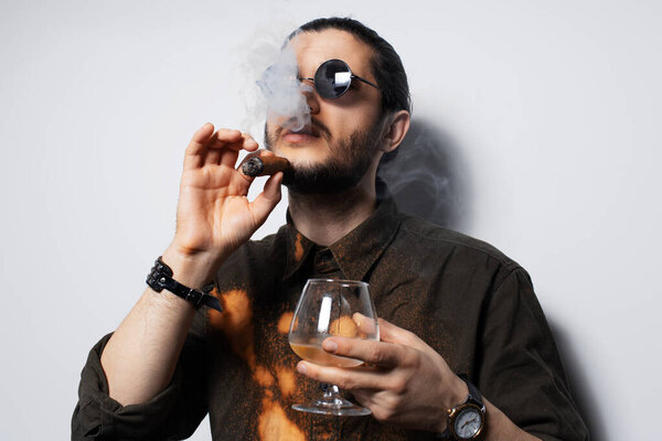 Studio portrait of young man with a cigar and whiskey on white background.