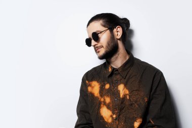 Beyaz arka planda yuvarlak güneş gözlüğü takan genç adamın yan portresi..