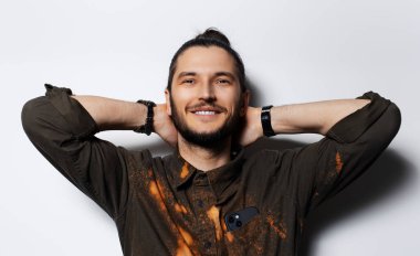 Elleri başının arkasında gülümseyen genç adamın stüdyo portresi..