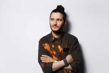 Saçlı çörekli genç adamın beyaz arka planda başka bir tarafa bakan stüdyo portresi..