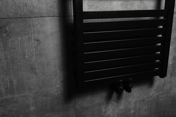 Close-up of black heated towel rail, in the bathroom with dark grey walls.
