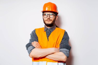 Çapraz kollu kendinden emin mühendis, beyaz üzerine turuncu ekipman giyiyor..