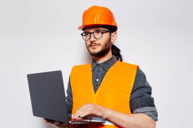Turuncu inşaat ekipmanlarında dizüstü bilgisayar tutan mühendisin stüdyo portresi..