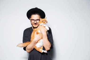 Siyah şapkalı, elinde tatlı kırmızı bir kedi tutan çekici bir adamın stüdyo fotoğrafı..
