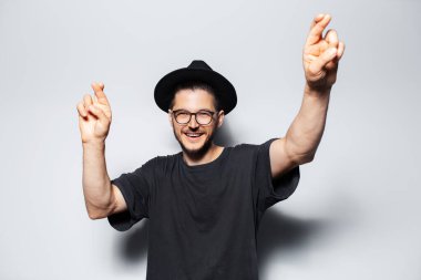 Mutlu genç adamın portresi gri stüdyo arka planında şans diliyor..