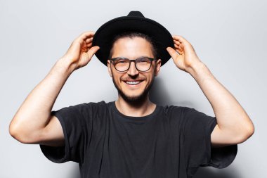 Gri stüdyo arka planında kafasından şapka tutan mutlu genç adamın portresi..