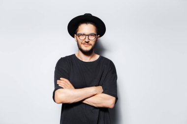 Siyah şapka ve gözlük takan çapraz kollu bir gencin stüdyo portresi..