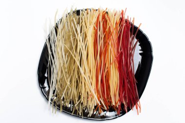 Siyah tabakta farklı renkte, beyaz arkaplanda ham makarnanın üst görünümü.