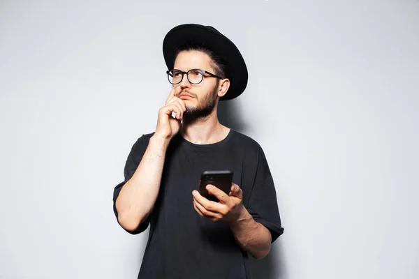 Portrait of thoughtful man with smartphone in hand on grey studio background.