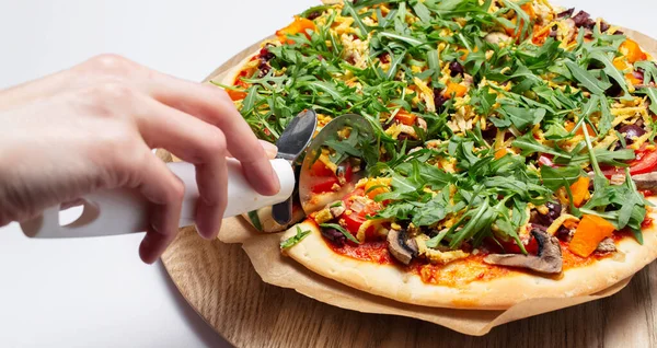 Vejetaryen ev yemeği. Pizzayı ahşap tabakta kesen kadının yakın çekimi..