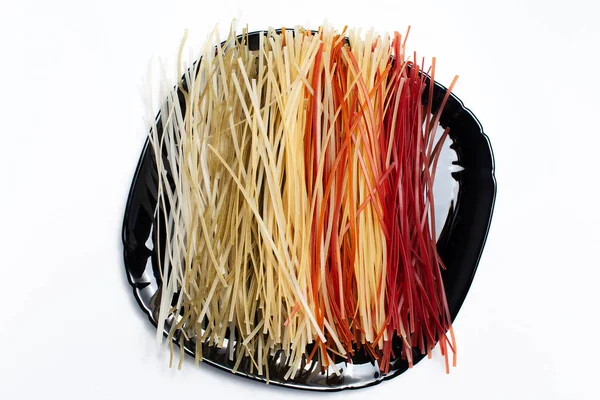 Siyah tabakta farklı renkte, beyaz arkaplanda ham makarnanın üst görünümü.