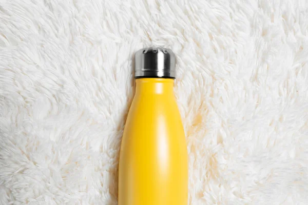 Close-up of steel reusable water bottle of yellow, on white fluffy plaid.