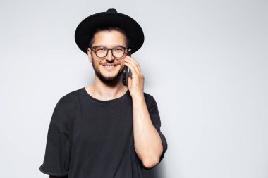 Açık gri arka planda akıllı telefondan konuşan genç adamın stüdyo portresi.