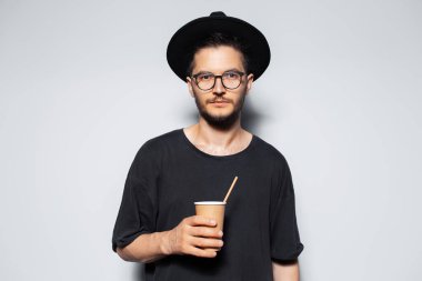 Gri arka planda elinde bir fincan kahve tutan genç adamın stüdyo portresi..