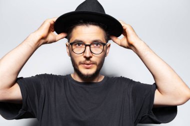 Gri stüdyo arka planında kafasından şapka tutan kendine güvenen adamın portresi..